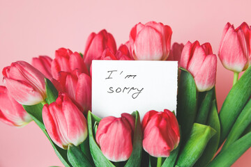 white card with the inscription i am sorry in a bouquet of beautiful tulips, the concept of apologies