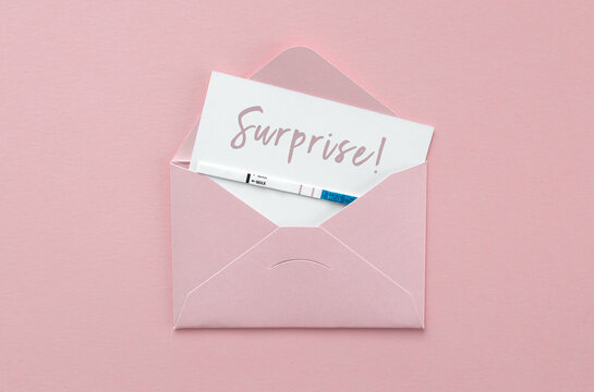 positive pregnancy test in pink envelope on pink background, postcard with inscription surprise, pregnancy concept.