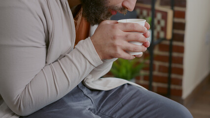 Close up of man shaking and drinking cup of coffee at aa therapy session. Adult with addiction trembling, holding beverage and attending rehabilitation meeting with psychiatrist.