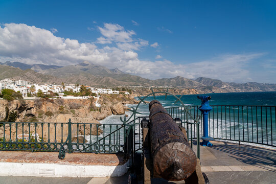 Rusty cannon at viewpoint of Europe's balcony in Nerja, Andalusia province, Spain. In background the city of Nerja and the Sierra Nevada mountains. Cloudy day.