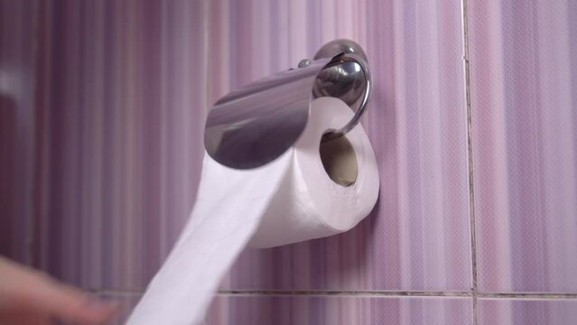 This close up video shows anonymous hands of someone suffering from diarrhea as they frantically pull toilet paper from dispenser.