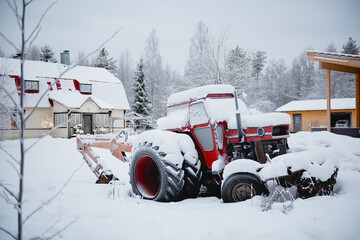 Tractor covered with the snow standing in the yard of the farm.