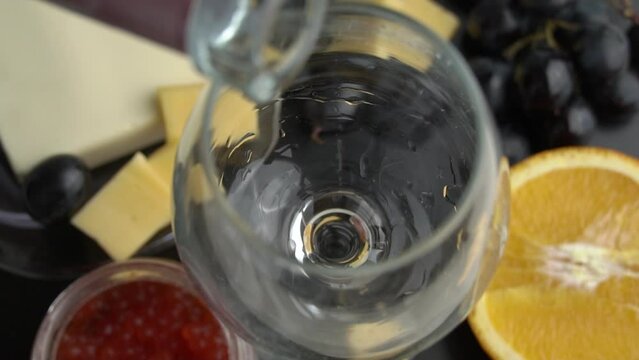 Rose wine is poured into a glass with appetizers in slow mo. Aesthetics of wine with cheese. Alcohol, romance, evening. Cheese, butter, red caviar, grapes, baguette, orange. View from above.