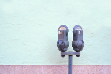 Two old metal parking meters, with a slot for coins, stand outdoors in front of a green plastered...