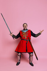 One young man, medieval warrior or knight wearing wearing armor clothing posing isolated over pink background. Comparison of eras, history, wow emotions - obrazy, fototapety, plakaty