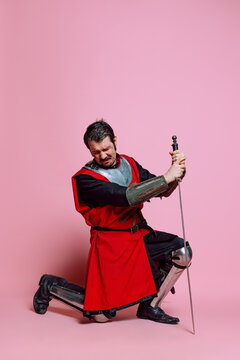 Crying young man, medieval warrior or knight wearing wearing armor clothing posing isolated over pink background. Comparison of eras, history, emotions