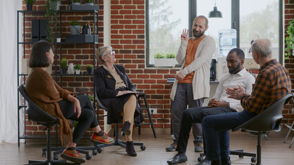 Happy man sharing progress and overcoming addiction with group of patients at aa meeting, celebrating together. People clapping hands and feeling glad about achievement at therapy session.