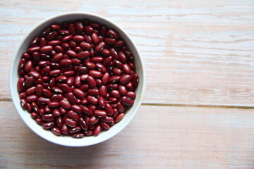 Red beans in a white crockery bowl on a wooden table, top view.