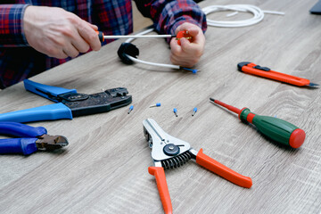 A male electrician changes the plug on an electric wire. Working with electrical tools. Stripper, crimp, screwdriver, wire cutters. Electrician connecting wires