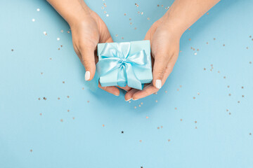 A hand holds a blue gift box on a blue background with glitter stars. top view, copy space