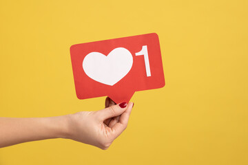 Support interesting web content, push heart button. Closeup of woman hand holding social media like icon, emoji sign to follow subscribe blog. Indoor studio shot isolated on yellow background.