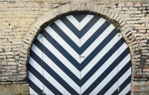 An old historic wooden gate that is in a round arch of an old city wall in Europe. The gate is painted black and white.