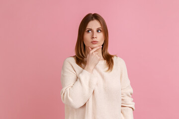 Portrait of blond woman standing deep in thoughts with puzzled serious doubtful face expression, making difficult decision, wearing white sweater. Indoor studio shot isolated on pink background.