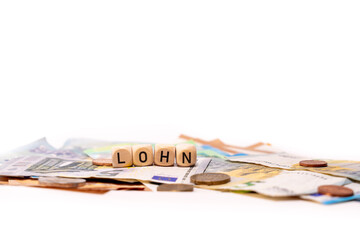 German word for wage, LOHN, spelled with wooden letters wooden cube on a plain white background with banknotes and coins, concept image