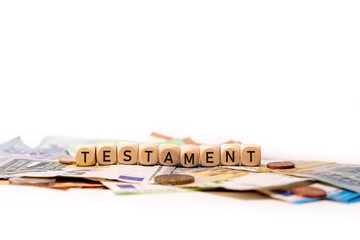 German word for testament, TESTAMENT, spelled with wooden letters wooden cube on a plain white background with banknotes and coins, concept image