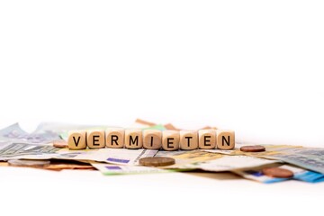 German word for rent out, VERMIETEN, spelled with wooden letters wooden cube on a plain white background with banknotes and coins, concept image