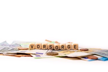 German word for Precaution, VORSORGE, spelled with wooden letters wooden cube on a plain white background with banknotes and coins, concept image