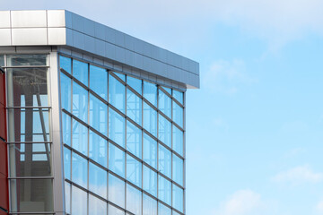 A fragment of the facade of a modern building made of glass and concrete against a blue sky.