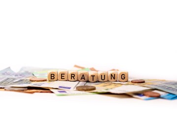 German word for consulting, BERATUNG, spelled with wooden letters wooden cube on a plain white background with banknotes and coins, concept image