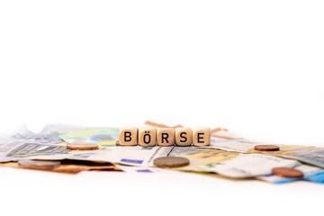German word for Stock market, BÖRSE, spelled with wooden letters wooden cube on a plain white background with banknotes and coins, concept image