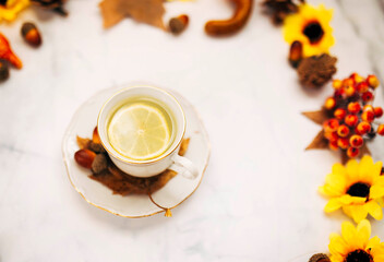 Obraz na płótnie Canvas Top view of a ceramic cup of lemon tea surrounded pine cones and autumnal maple leaves. Focus on lemon.