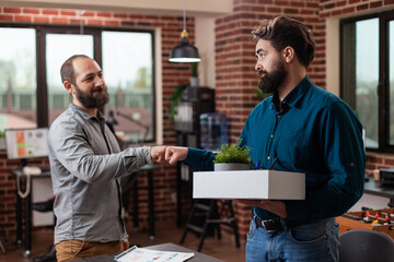 Fototapeta na wymiar Executive manager punching fist with sad fired entrepreneur man while carrying his box with belongings after being fired. Multiracial businesspeople working at company strategy in startup office