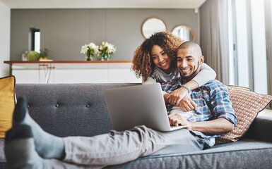 Theres no denying their connection. Shot of a young woman hugging her husband while he uses a laptop on the sofa at home.