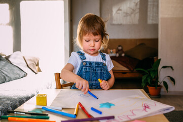 Small child at home at the children's table draws with felt-tip pens.