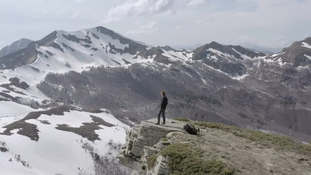 Hiker standing on high mountain peak admiring view on mountains covered in snow