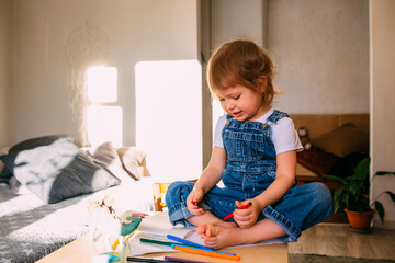 Small child at home at the children's table draws with felt-tip pens.