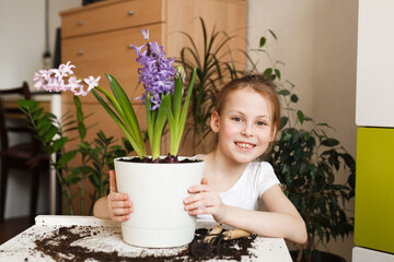 Close-up portrait of a happy smiling girl doing home gardening in a room with houseplants. Plant care, children's leisure activities and hobbies, domestic life.