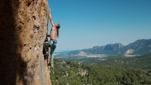 Fit man rock climbing up mountain focusing on his next move, reaching rock holds. cinematic slow motion, fitness and healthy active lifestyle