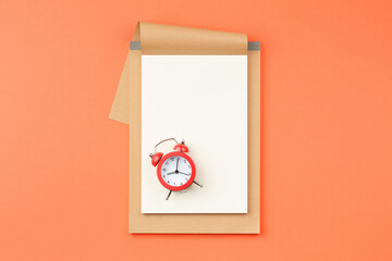 Open notebook and alarm clock on orange background