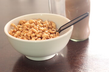 cereal in a white cup with chocolate milk in a ready-to-eat glass jar Served on a brown wooden table.