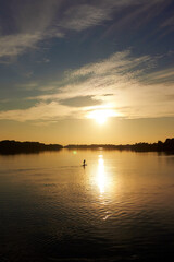Sporty woman on paddle board at quiet river near ship with colorful sunset or sunrise