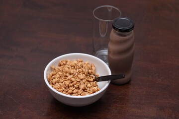 cereal in a white cup with chocolate milk in a ready-to-eat glass jar Served on a brown wooden table.
