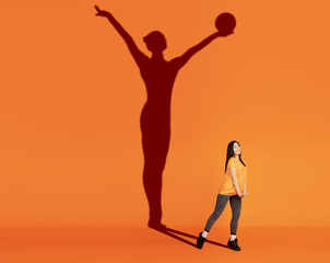 Young pretty girl dreams of becoming gymnast isolated on orange background. Sport, career and...