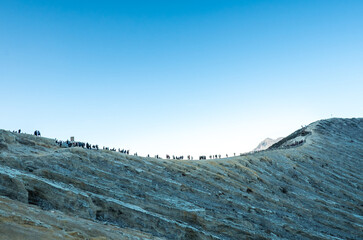 Many people hiking on top of mountain or volcano. Tourists walking in the crater of a active volcano with blue sky