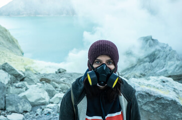 Young adventurous woman wearing respirator protective mask hiking on mountain or volcano. Female tourist in the crater of a active volcano with fumes
