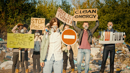Young Generation Care About the Future. Group of Young Volunteers in Gas Masks With a Poster Calling to Take Care of the Environment While Going Trough at Garbage Dump.