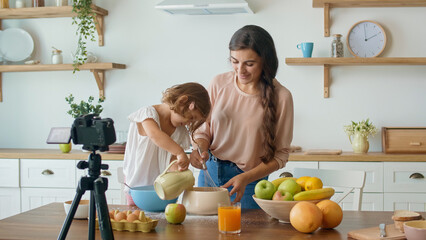 A Pretty Mother With a Cute Daughter Shooting a Blog About Cooking. Video Blog About Healthy Food. Mother and Daughter Cooking Together on the Camera. A Mother With Child Streaming Online Video Vlog.