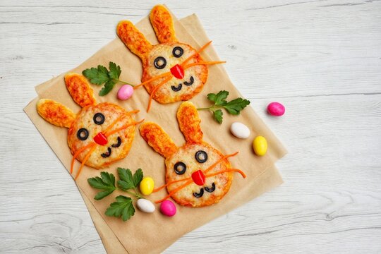 Selective focus on mini easter bunny pizzas on parchment paper with white wood background.Art food idea for kids Easter's party.Top view.Copy space