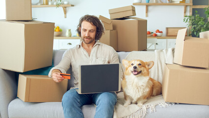 A Man Uses a Laptop For Online Shopping at Home. Purchase Confirmation by the Internet. Binding a Card for Online Shopping. A Man Sitting on the Couch With a Cute Dog While Online Shopping.