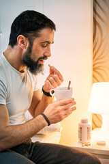 person with some kind of problem sitting on the bed and taking a pill, vertical view.