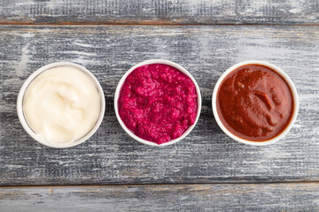 ceramic sauce bowls with horseradish, tomato sauce and mayonnaise on a gray. Top view, copy space.