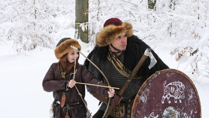 Father viking teach his son to archery in the winter forest. They dressed in medieval clothes.