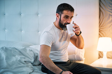 person with some kind of problem sitting on the bed and drinking from a cup