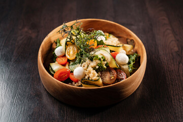 Salad with vegetables, cheese and herbs in a deep wooden plate.