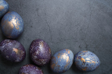 Easter card with a copy of the place for the text. Purple, blue and golden eggs on a dark background. The trend of 2022 purple shade is very peri. Natural dye karkade tea. Top view.