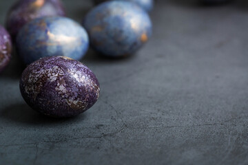 Easter card with a copy of the place for the text. Purple, blue and golden eggs on a dark background. The trend of 2022 purple shade is very peri. Natural dye karkade tea. Top view.